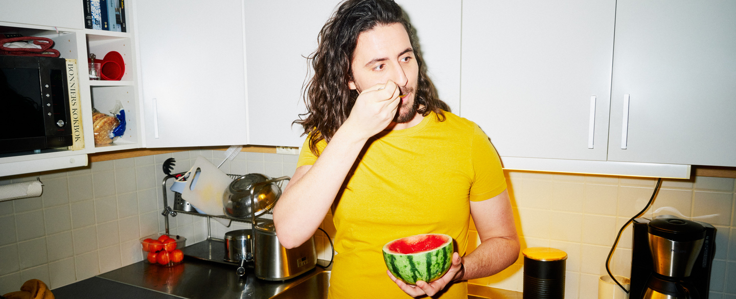kille med gul tröja står i köket och äter en melon med en sked
