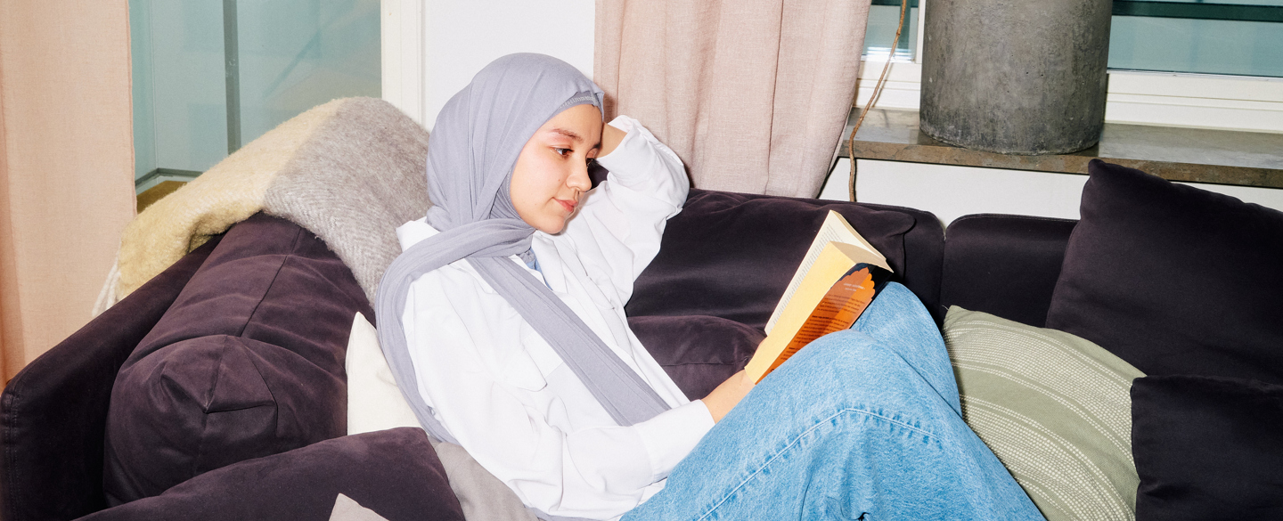 ung tjej med slöja sitter på soffan och läser en bok
